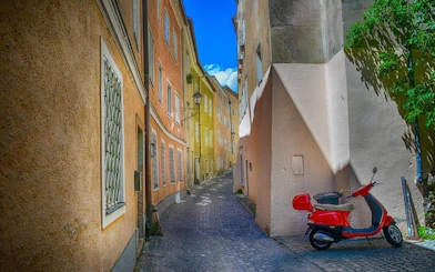 Narrow cobblestone street in Salzburg with colorful buildings and a red scooter.