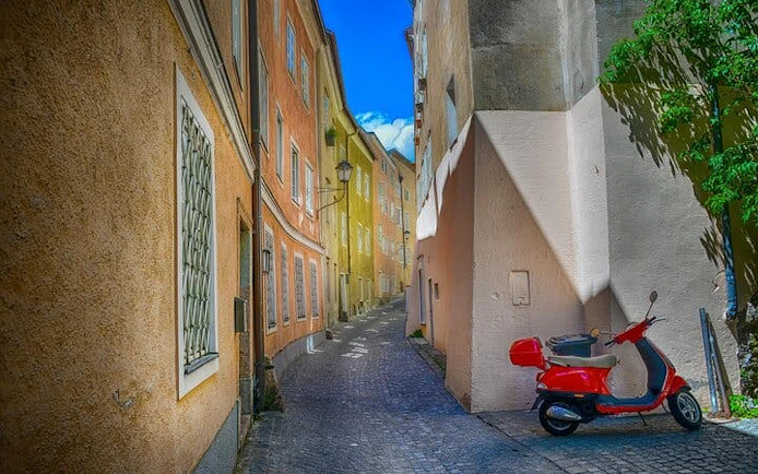 Narrow cobblestone street in Salzburg with colorful buildings and a red scooter.
