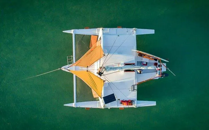 Catamaran sailing in Punta Cana with orange sails, viewed from above, on turquoise water.