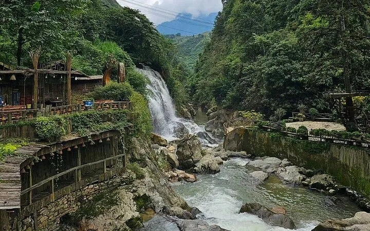 Waterfall and wooden bridge in lush Sapa village landscape, Vietnam.