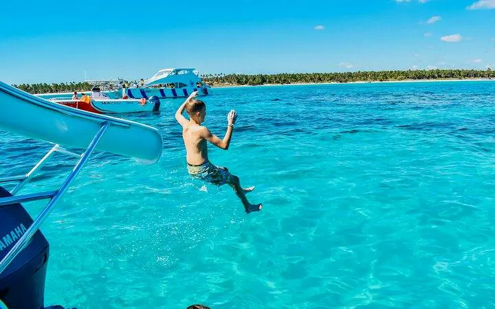 Child jumping off catamaran slide into turquoise water, Punta Cana snorkeling cruise.