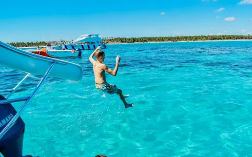Child jumping off catamaran slide into turquoise water, Punta Cana snorkeling cruise.