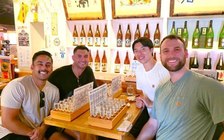 Group enjoying sake tasting at Fushimi brewery in Kyoto, surrounded by sake bottles.