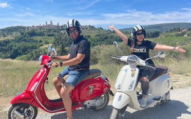 Tourists riding Vespas with San Gimignano in the background on a Chianti tour.