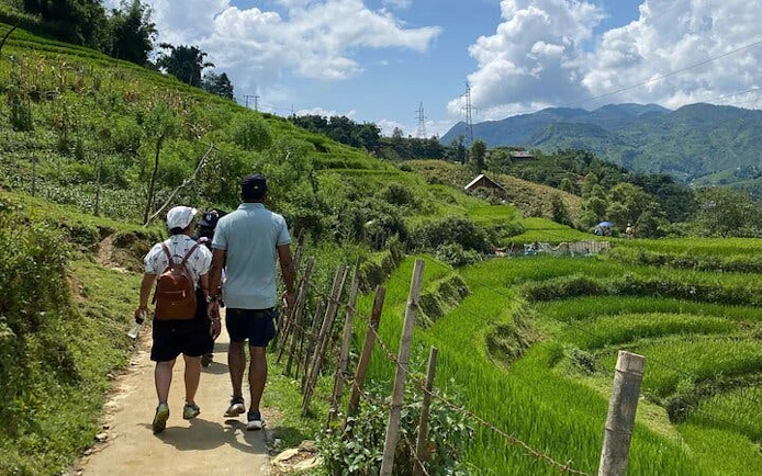 Tourists trekking on Sapa's Y Linh Ho trail with lush rice terraces and mountains in the background.