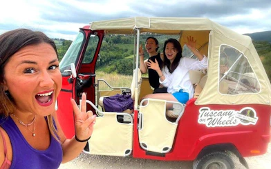 Tuk Tuk tour in Tuscany with guide and passengers, scenic countryside backdrop.