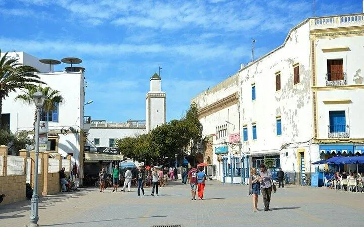 Essaouira city square with people walking, featuring traditional buildings and a minaret.