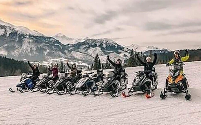 Snowmobilers in Zakopane with mountain backdrop during guided adventure tour.