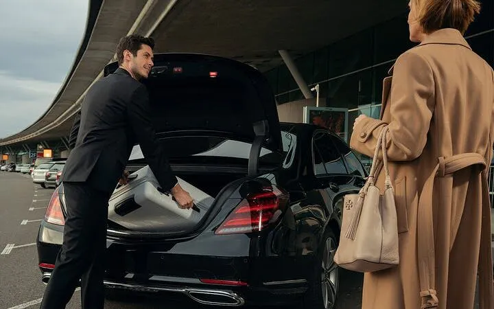 Man loading suitcase into black car trunk at airport for Hurghada hotel transfer.