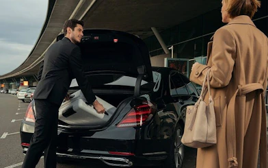 Man loading suitcase into black car trunk at airport for Hurghada hotel transfer.