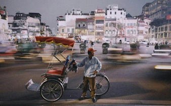 Cyclo driver in Hanoi Old Quarter at dusk with blurred city lights.
