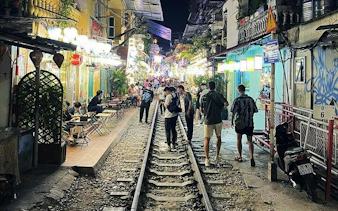 Hanoi street with people walking along train tracks, vibrant night market atmosphere.