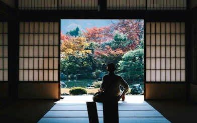 Person sitting in traditional Japanese room overlooking a garden with autumn foliage in Kyoto.