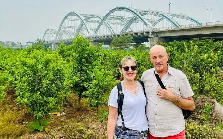 Couple standing in front of lush greenery with a bridge in Hanoi countryside during Vespa tour.