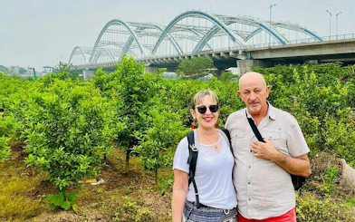 Couple standing in front of lush greenery with a bridge in Hanoi countryside during Vespa tour.
