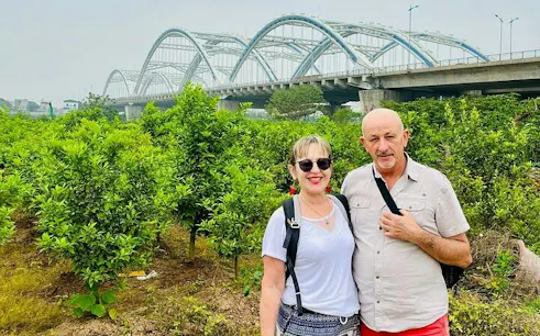 Couple standing in front of lush greenery with a bridge in Hanoi countryside during Vespa tour.