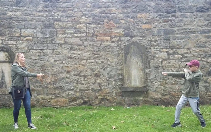 Tour participants reenacting a wizard duel in front of a historic stone wall in York.