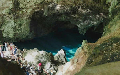 Tourists exploring a cave with a blue underground pool in Santo Domingo, part of a guided day tour from Punta Cana.