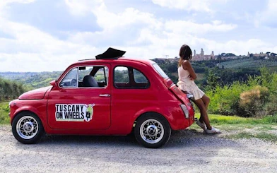 Red vintage Fiat 500 parked with view of San Gimignano skyline in Tuscany.