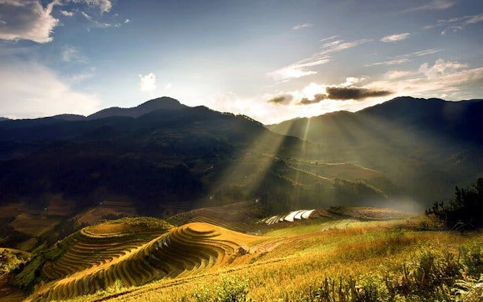 Terraced rice fields in Mu Cang Chai with sun rays over mountains, Vietnam.
