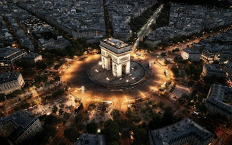 Arc de Triomphe illuminated at night with view of Paris streets and cityscape.