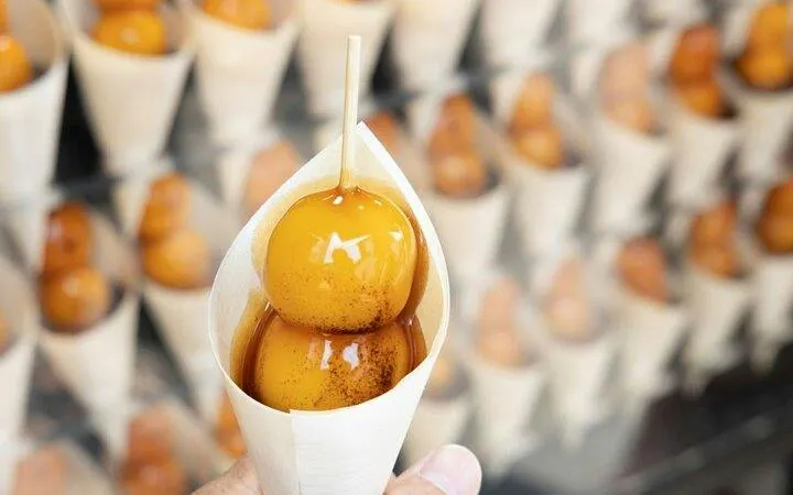 Dango skewers in a paper cone at a Kyoto street food stall during Arashiyama walking tour.