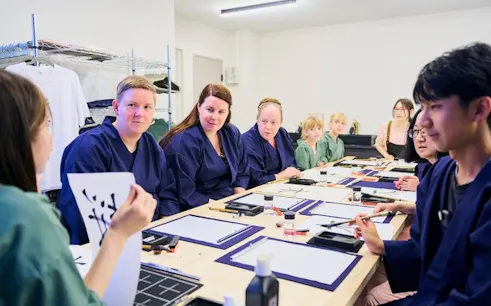 Participants in a Shinjuku calligraphy workshop in Tokyo, learning techniques around a table.