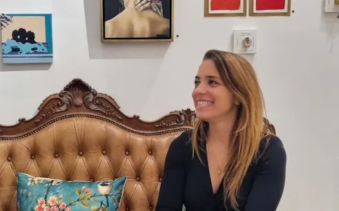 Lisbon artist's studio with paintings on wall and woman seated on vintage sofa.