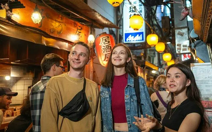 Tourists exploring Shinjuku's vibrant alley with a local guide, Tokyo food tour.