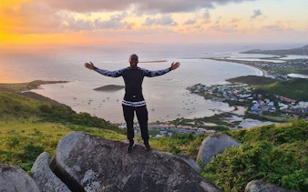 Man standing on a rock with arms outstretched, overlooking St. Maarten's coastline at sunset.