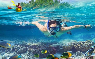 Snorkeler exploring coral reef with tropical fish, kayaker in background, Ang Thong National Marine Park.
