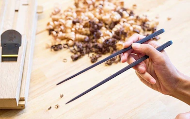 Hand crafting chopsticks at Kyoto Arashiyama workshop with wood shavings in background.