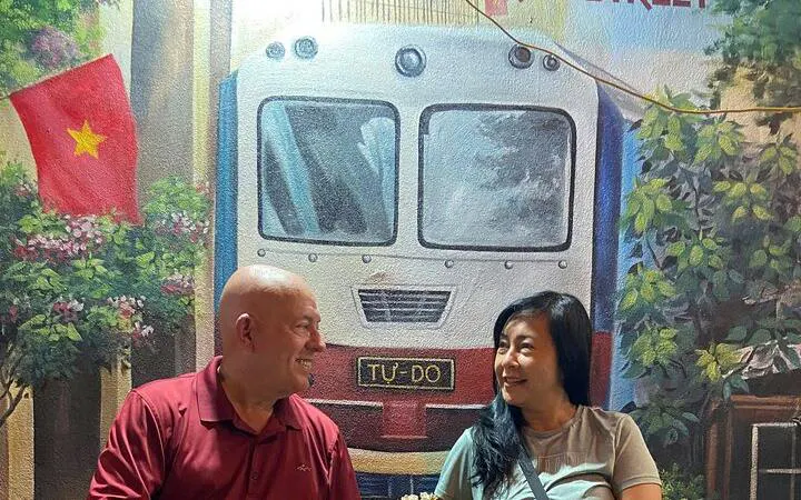 Couple enjoying Hanoi nightlife with train mural backdrop.