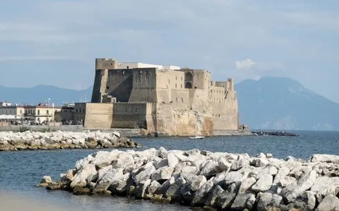 Castel dell'Ovo on the waterfront in Naples, Italy, with Mount Vesuvius in the background.