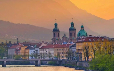 Innsbruck cityscape with historic buildings and church domes at sunset, view from the river.