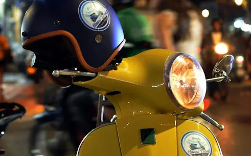 Yellow Vespa with helmet on Hanoi street, capturing night tour ambiance.