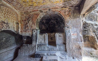 Ancient rock-cut church interior in Cappadocia with frescoes and stone altar.