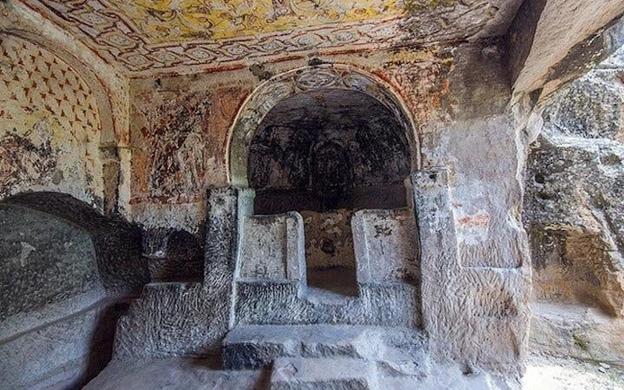 Ancient rock-cut church interior in Cappadocia with frescoes and stone altar.