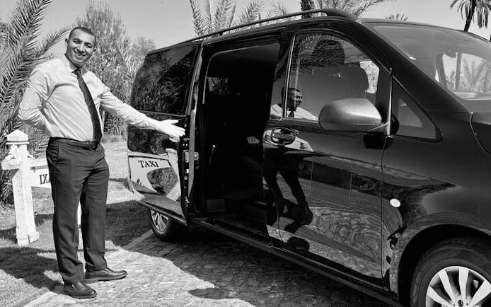 Man standing next to a taxi van for private transfer service between Taghazout and Marrakesh.