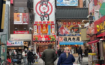 Dotonbori street scene with people exploring vibrant food stalls and colorful signage in Osaka, Japan.