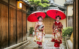 Geisha walking with red umbrellas in Kyoto's Gion district.