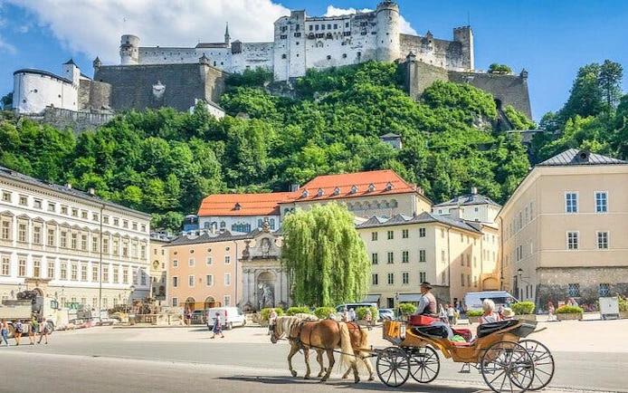 Salzburg fortress view with horse-drawn carriage in historic city square.