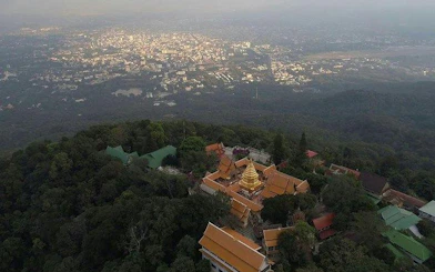 Aerial view of Wat Phra That Doi Suthep temple surrounded by forest, overlooking Chiang Mai city.