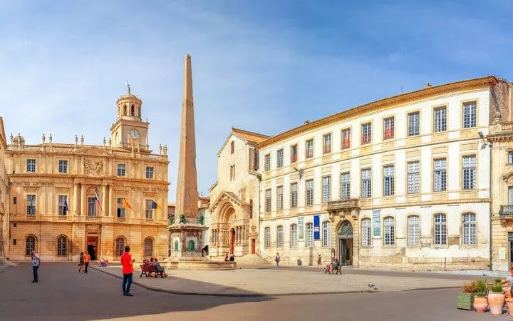 Arles city square with obelisk and historic buildings on self-guided walking tour.