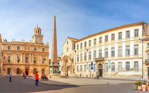 Arles city square with obelisk and historic buildings on self-guided walking tour.