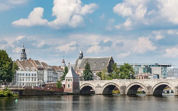 Maastricht stone bridge over river with historic buildings in background.