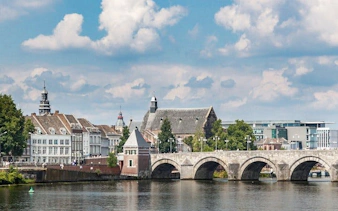 Maastricht stone bridge over river with historic buildings in background.