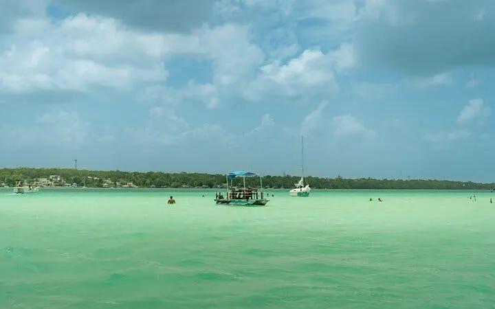 Pontoon boat on Bacalar Lagoon with swimmers, cloudy sky, and distant shoreline.