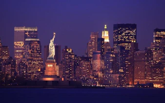 Statue of Liberty with New York City skyline at dusk, featured in self-guided walking tour app.