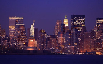Statue of Liberty with New York City skyline at dusk, featured in self-guided walking tour app.